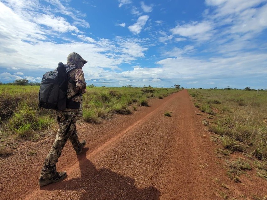 Adam Rainoff camina por un sendero de tierra roja, vestido de camuflaje