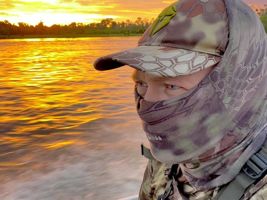 Adam Rainoff en una lancha al atardecer, con ropa de camuflaje