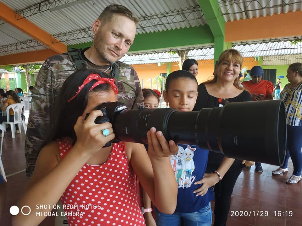 Children look through Adam's Pentax and long lens at a community event, January 2020